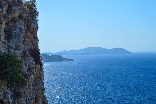 Part of the ancient Monolithos Castle in Rhodes, Greece, this image captures the weathered stone walls of the fortress standing tall above a lush forest, with sweeping views of the Aegean Sea and coastline in the background. Built by the Knights of Saint John in the 15th century, this historic castle was strategically placed for defense and surveillance. The photo highlights the contrast between rugged medieval architecture and the vibrant natural landscape, under a radiant blue sky