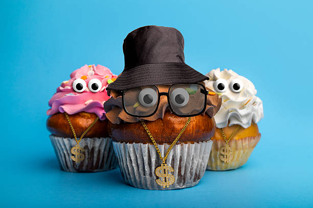 Three funny cupcakes on a blue background with googly eyes dressed in 80s style hip hop rapper attire.