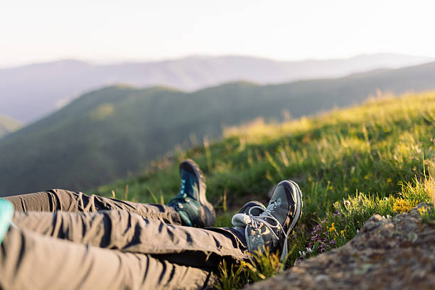 Two mature women taking a break from hiking to admire the view. Their backpacks backpacks and trekking poles are next to them. The nature around them is amazing, it's a beautiful spring sunny day.