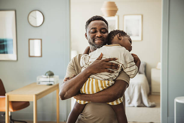 Loving and caring African American father giving a hug to his toddler son at home.