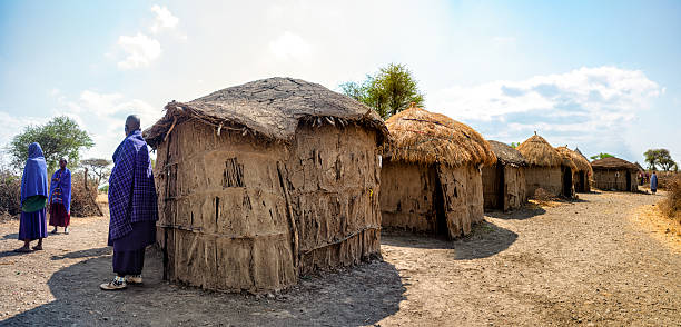 September 26, 2024 - makuyuni, Arusha, Tanzania: Maasai villagers are standing near their traditional mud houses with thatched roofs in a rural area of Tanzania, showcasing their unique way of life