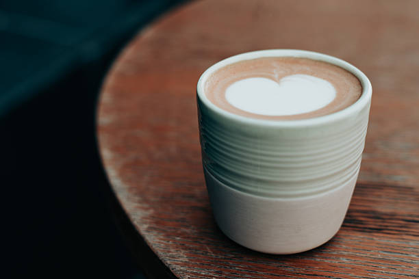 A warm latte featuring a heart-shaped design rests on a wooden table. Morning hot drink.