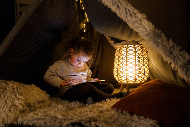 istock A Little Girl Using Digital Tablet in Cozy Blanket Fort 2216580032