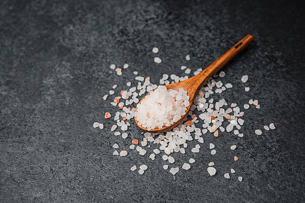 istock Wooden spoon filled with pink himalayan salt on textured black surface 2216581578