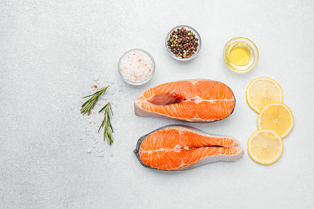istock Fresh salmon fillets with lemon slices, herbs, and spices on kitchen counter 2216581603