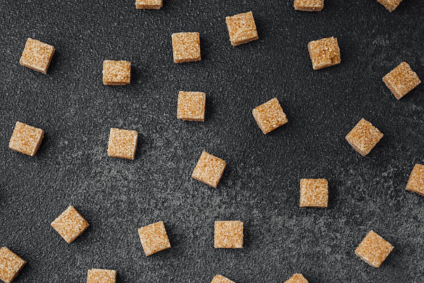 istock Sweet brown sugar cubes scattered on a dark textured surface 2216581616