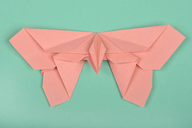 A pink paper origami butterfly with intricate folds is positioned on a light teal surface