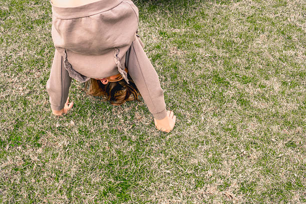 Young girl performing a handstand on a lush grassy field, embracing the joy of play and freedom outdoors. Sunlight illuminating her carefree spirit and active energy