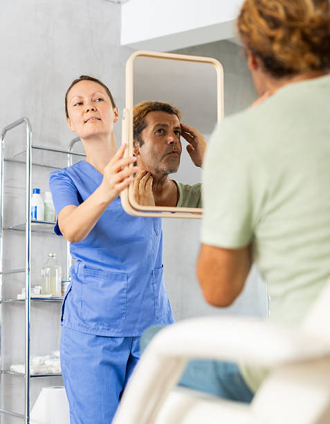 istock Man scrutinizing his own reflection in mirror held by female cosmetologist 2216606001