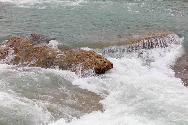 A waterfall with a greenish tint. The water is white and the rocks are brown. The water is flowing down the rocks and creating a misty atmosphere