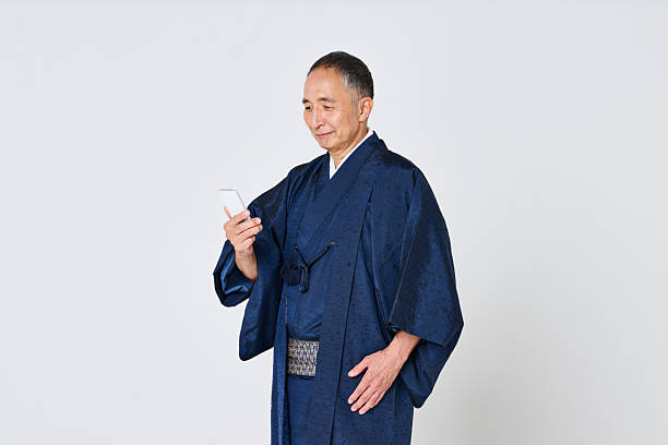 istock Senior man wearing a navy blue kimono using a smartphone 2216609009
