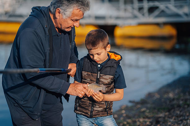 Grandfather and grandson admiring a small fish caught in the river, sharing a special moment together in nature