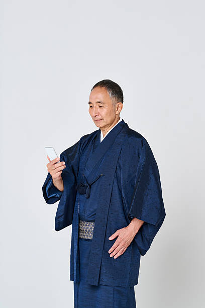 istock Senior man wearing a navy blue kimono using a smartphone 2216610499