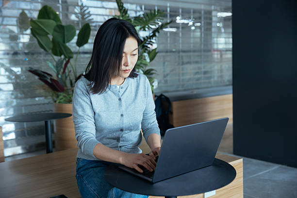 istock Young Asian woman working on laptop while sitting in office lobby 2216613689