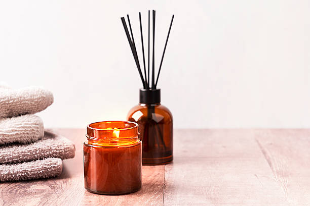 Cozy spa ambiance with glowing candle, aromatic reed diffuser and folded towels with copy space