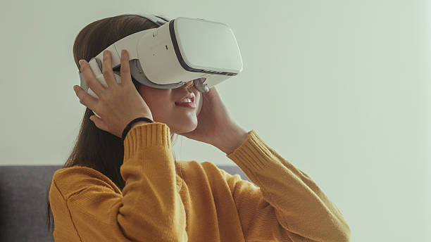 istock Young woman using virtual reality headset at home, looking upward with excitement. Represents immersive experience, future technology, digital lifestyle, and interactive entertainment. 2216619143