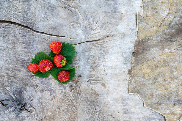 Red strawberry with green leaves on a wooden background with copy space.