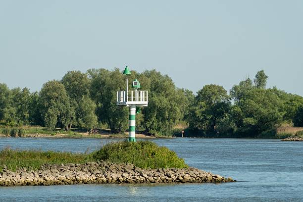 Green and white river signal standing on a small island, guiding ships on a sunny day