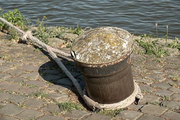 Aged bollard with rope on cobblestone near the water