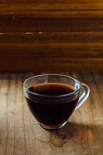 A glass cup filled with dark coffee sits on a rustic wooden table. The warm beverage invites moments of relaxation and comfort in a cozy atmosphere.
