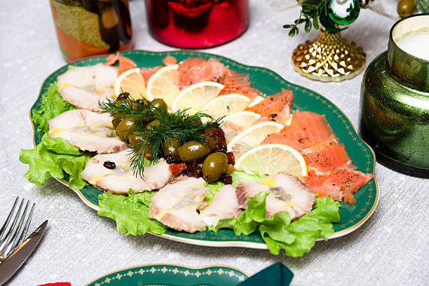 Elegant holiday platter with smoked fish slices, lemon wedges, green olives, herbs, and lettuce served on a festive table.