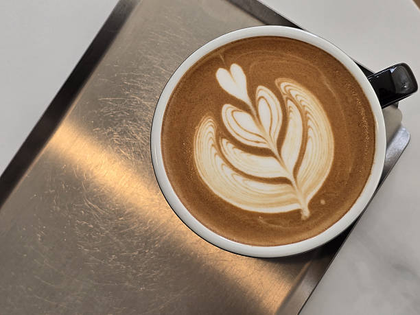 istock beautifully crafted latte with intricate foam art sits in black cup on metallic surface, showcasing heart and leaf design that adds artistic touch to beverage 2216642501