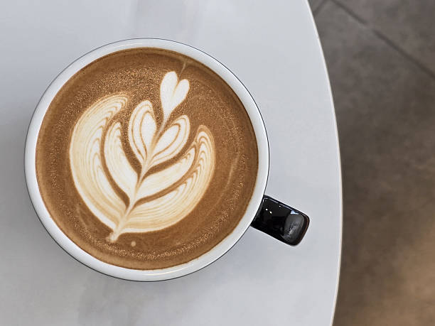 istock beautifully crafted latte with intricate foam art, featuring leaf design, sits in black cup on white table. warm tones of coffee create cozy atmosphere 2216642512