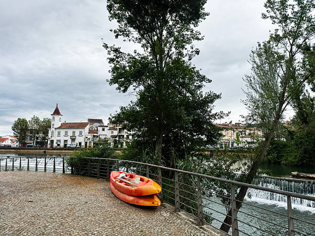 istock Riverside scene in Tomar with kayaks, trees, and historic architecture 2216644541