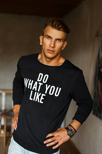 istock Stylish handsome young man in a black pullover with print words in the room 2216646122
