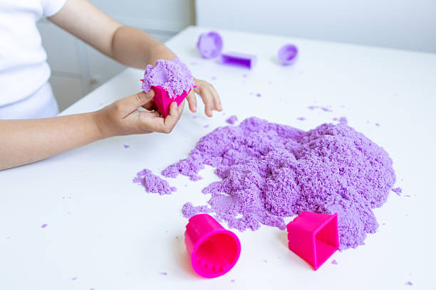 istock Child playing with purple kinetic sand and pink molds on white table 2216646458
