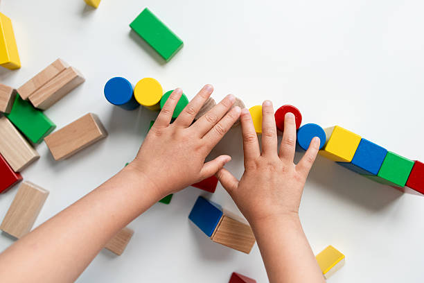 istock Child hands building colorful wooden block tower on white surface 2216647101