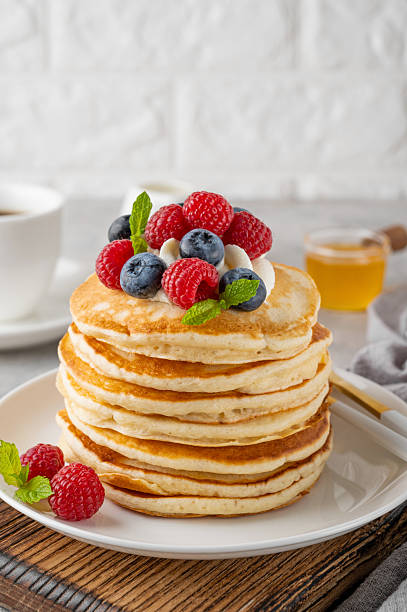 istock A stack of pancakes with whipped cream, fresh berries and honey on a white plate on a gray concrete background. 2216648609