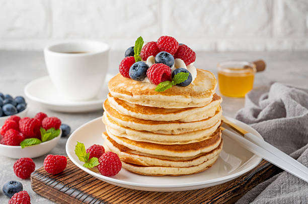 istock A stack of pancakes with whipped cream, fresh berries and honey on a white plate on a gray concrete background. 2216648650