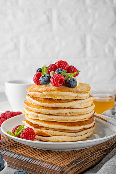 istock A stack of pancakes with whipped cream, fresh berries and honey on a white plate on a gray concrete background. 2216648670