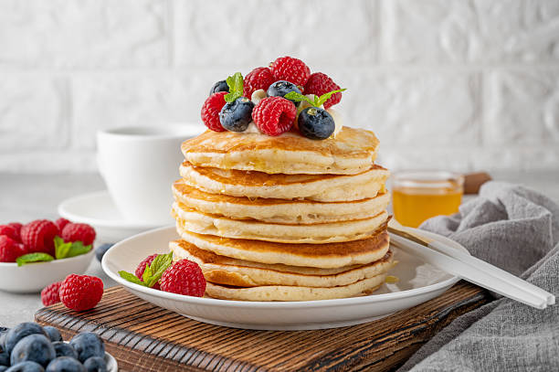istock A stack of pancakes with whipped cream, fresh berries and honey on a white plate on a gray concrete background. 2216648679