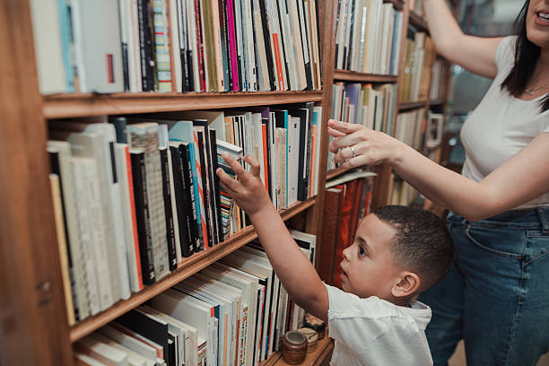 African, child and mother looking for a book on the shelves at home