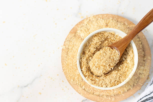 istock Nutritional yeast flakes in a bowl with wooden spoon on white kitchen table 2216650009