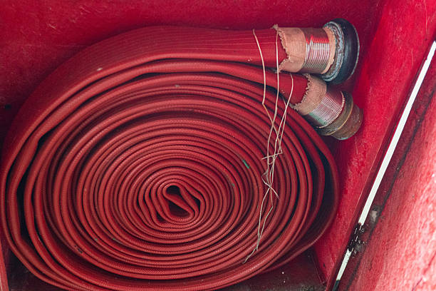 Close-up of a tightly coiled red fire hose inside a bright red cabinet, ready for emergency deployment.