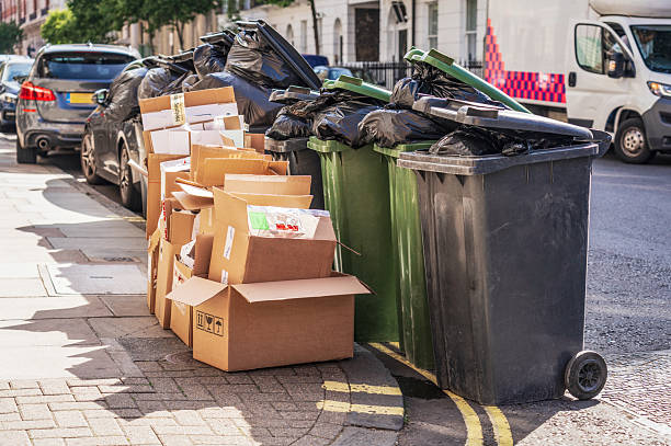 Wheelybins and cardboard ready for collection Several black and green wheel bins full of rubbish bags, alongside a collection of cardboard boxes for recycling on a residential street in London. overflowing trash dumpster stock pictures, royalty-free photos & images