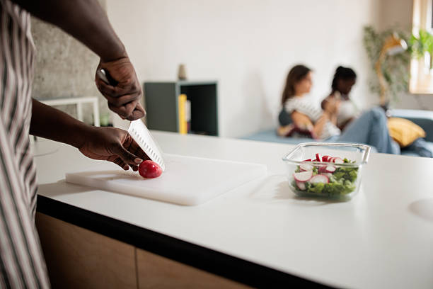 Black man slicing ingredients and assembling a colorful salad in his contemporary apartment kitchen for him and his friends.