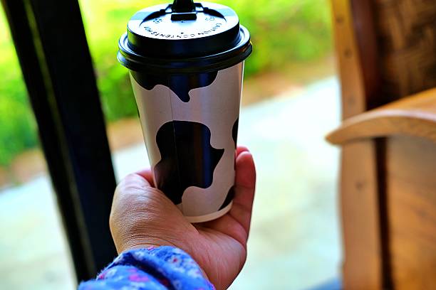 A stylish disposable coffee cup with cow pattern held indoors, perfect for trendy café culture and lifestyle content.