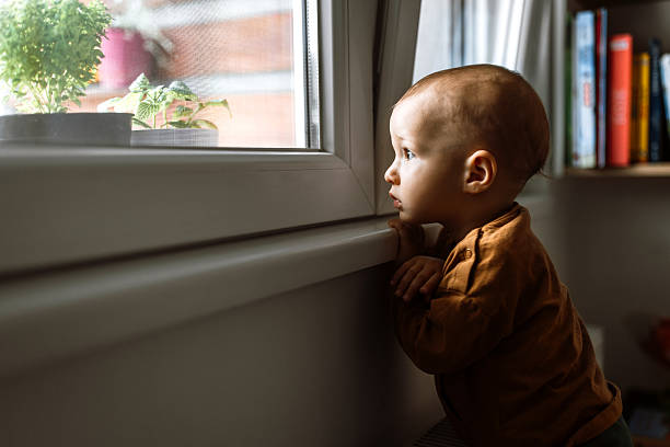 istock Cute baby boy standing next to the window, looking away 2216662459