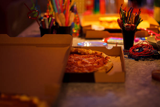 Close-up of a pizza in a box surrounded by colorful party items, suggesting a lively celebration atmosphere with food, decorations, and cheerful vibes.