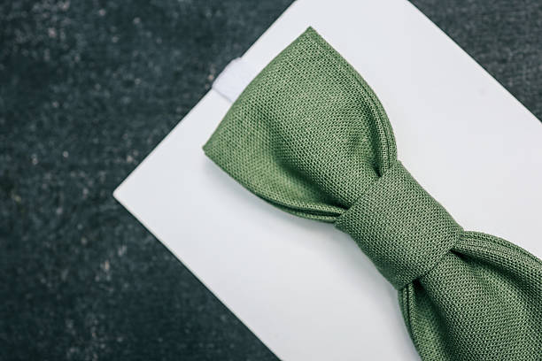 Green linen bow tie on white card background, presented on dark textured surface. Stylish accessory for kids or formal wear, captured in minimalist flatlay composition.