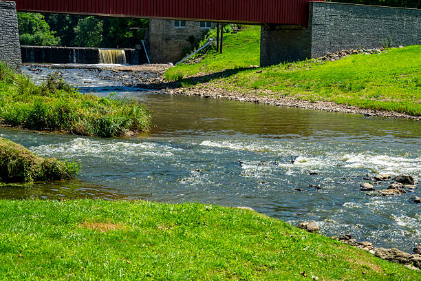 istock Beautiful River Flowing Beneath a Red Covered Bridge in a Serene Landscape During a Sunny Day 2216672788