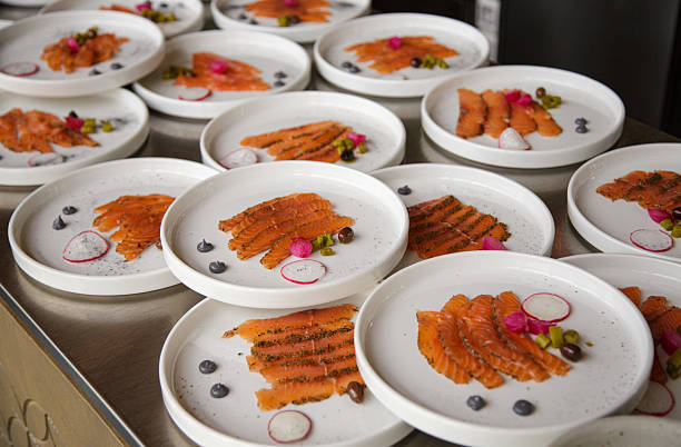 A collection of elegantly plated smoked salmon appetizers arranged on white dishes, garnished with fresh radish slices, capers, and possibly herbs or sauce. This high-angle shot highlights the sophisticated presentation of the gourmet food, perfect for illustrating concepts of fine dining, catering, appetizers, healthy eating, and culinary artistry.