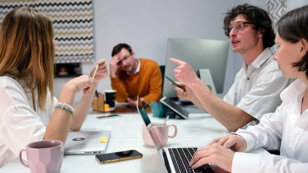 A tired boss listens to the ideas of his creative team. Several people are sitting at a table and discussing the work on a project A tired boss listens to the ideas of his creative team. Several people are sitting at a table and discussing the work on a project. There are several laptops and cell phones on the table, as well as cups. tax planning discussion stock pictures, royalty-free photos  images