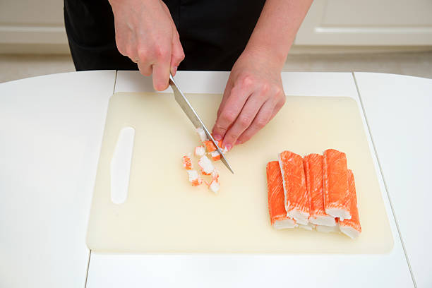 istock Close-up of hands cutting imitation crab sticks on a plastic cutting board, preparing ingredients for seafood salad or sushi rolls. 2216692411