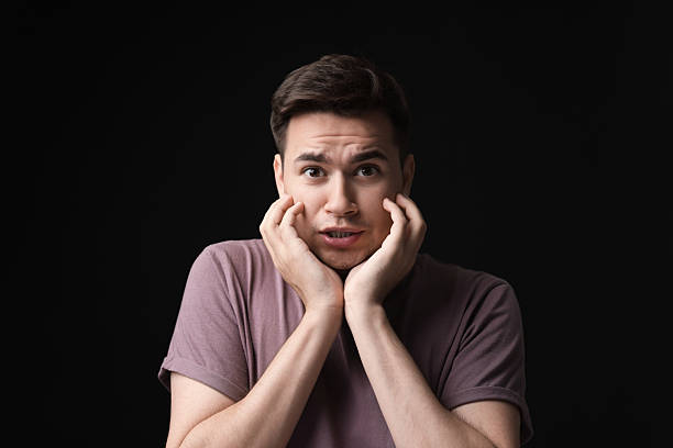 istock Portrait of scared young man on black background 2216692696