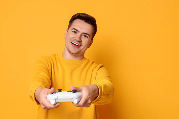 istock Happy young man playing video games with controller on orange background, space for text 2216692842